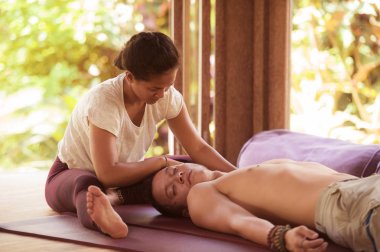 Genç, güzel ve egzotik Asyalı Taylandlı kadın. Geleneksel baş ve yüz masajı yapıyor. Beyaz bir adama.