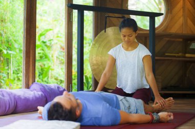 Genç, güzel ve egzotik Asyalı Balili sağlık terapisti, geleneksel bahçe bakım rahatlama konseptindeki beyaz adama Tayland masajı yapıyor.