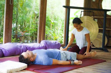 Genç, güzel ve egzotik Asyalı Balili sağlık terapisti, geleneksel bahçe bakım rahatlama konseptindeki beyaz adama Tayland masajı yapıyor.