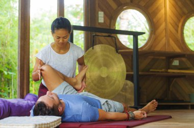 Genç, güzel ve egzotik Asyalı Balili sağlık terapisti, geleneksel bahçe bakım rahatlama konseptindeki beyaz adama Tayland masajı yapıyor.