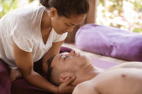 Joven hermoso y exótico asiático tailandés terapeuta mujer dando tradicional cabeza y facial balinés masaje a caucásico hombre en armonía salud cuidado y bienestar — Foto de Stock