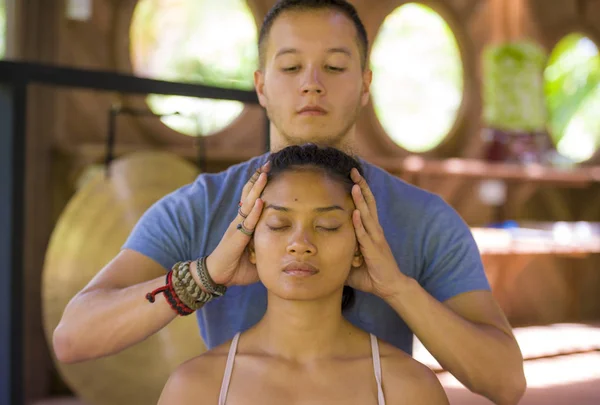 Natürliches Lifestyleporträt einer jungen schönen und entspannten asiatischen Balinesin, die eine heilende Gesichts- und Kopfthai-Massage von einem männlichen Therapeuten im traditionellen Spa erhält — Stockfoto
