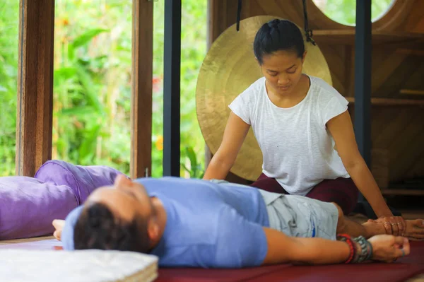 Genç, güzel ve egzotik Asyalı Balili sağlık terapisti, geleneksel bahçe bakım rahatlama konseptindeki beyaz adama Tayland masajı yapıyor.