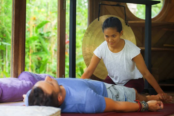 Genç, güzel ve egzotik Asyalı Balili sağlık terapisti, geleneksel bahçe bakım rahatlama konseptindeki beyaz adama Tayland masajı yapıyor.