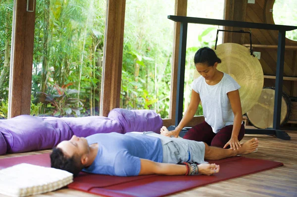 Genç, güzel ve egzotik Asyalı Balili sağlık terapisti, geleneksel bahçe bakım rahatlama konseptindeki beyaz adama Tayland masajı yapıyor.