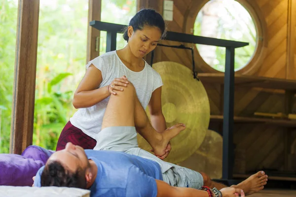 Joven hermosa y exótica asiática balinesa wellness terapeuta dando cuerpo tailandés masaje a atractivo caucásico hombre en tradicional jardín spa en salud cuidado relajación concepto —  Fotos de Stock