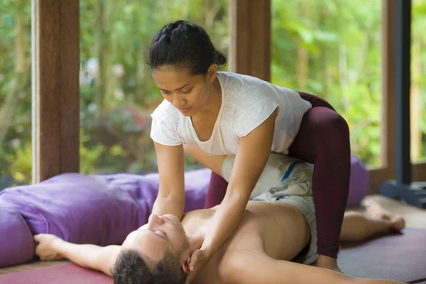 Mladá krásná a exotická asijská indonéská terapeutka žena dává tradiční thajskou masáž muži uvolněnému v tropických wellness lázních ve zdravém přírodním životním stylu — Stock fotografie