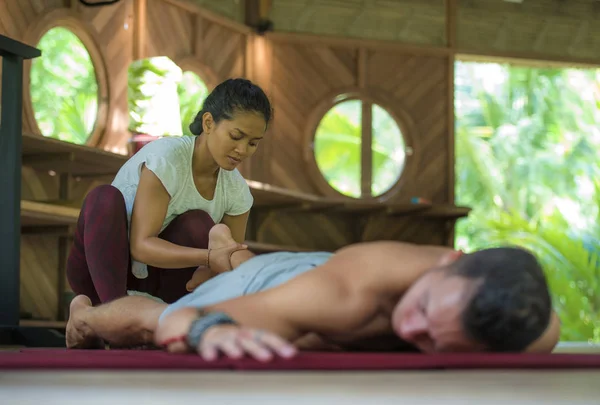 Молодая красивая и экзотическая азиатская индонезийская терапевт женщина делает традиционный тайский массаж мужчине расслабленным в тропическом оздоровительном спа-центре в здоровом естественном образе жизни — стоковое фото