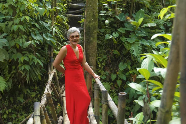 Estilo de vida natural retrato de hermosa y feliz de mediana edad de 40 o 50 años Mujer asiática con el pelo gris en vestido rojo elegante caminando sobre el paisaje verde de la selva tropical — Foto de Stock