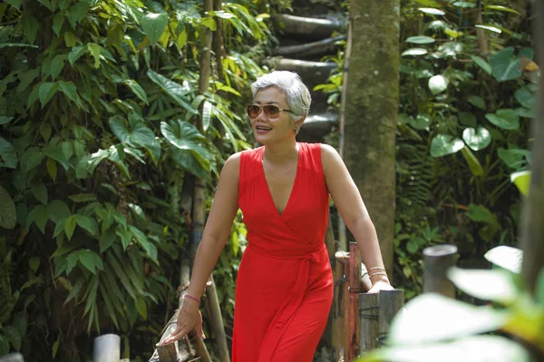 Estilo de vida natural retrato de hermosa y feliz de mediana edad de 40 o 50 años Mujer asiática con el pelo gris en vestido rojo elegante caminando sobre el paisaje verde de la selva tropical —  Fotos de Stock