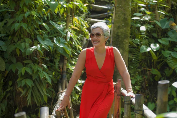 Retrato de estilo de vida natural de bela e feliz idade média 40 ou 50 anos Mulher asiática com cabelos grisalhos em vestido vermelho elegante andando na paisagem verde da selva tropical — Fotografia de Stock