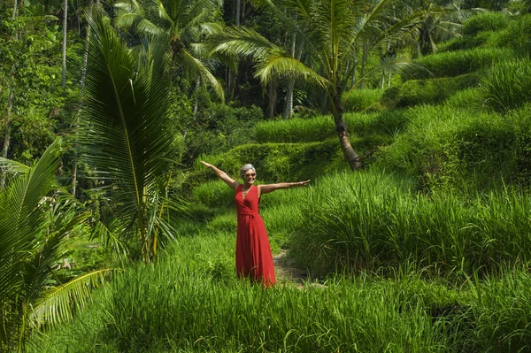 Natürliches Lifestyleporträt einer schönen und glücklichen asiatischen Frau mittleren Alters in den 40er oder 50er Jahren mit grauen Haaren in stylischem roten Kleid, die auf grünen tropischen Waldlandschaften wandelt — Stockfoto
