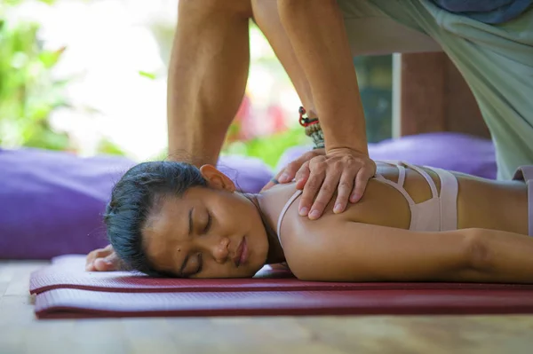 Joven hermosa y exótica mujer balinesa asiática tumbada en la estera del estudio recibiendo masaje tailandés tradicional por masajista en el jardín de spa de bienestar tropical en concepto de cuidado de la salud — Foto de Stock
