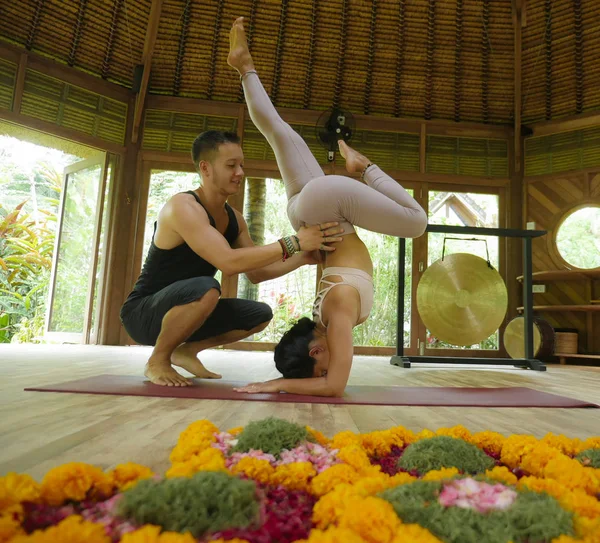 Genç, güzel ve zinde bir kadın ve akrobat bir adam yoga koçu olarak denge pozisyonunu öğreniyor. Egzotik jimnastik salonunda sağlık ve sağlıklı yaşam tarzında denge egzersizi yapıyor. — Stok fotoğraf