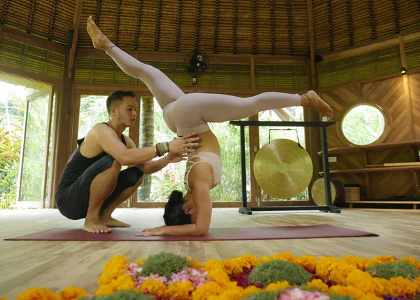 Genç, güzel ve zinde bir kadın ve akrobat bir adam yoga koçu olarak denge pozisyonunu öğreniyor. Egzotik jimnastik salonunda sağlık ve sağlıklı yaşam tarzında denge egzersizi yapıyor. — Stok fotoğraf