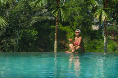 çekici ve mutlu orta yaşlı Asyalı kadın doğal yaşam tarzı portre orman arka plan ile tropikal tatil sonsuzluk simming havuzunda rahat bir içki rahat zevk