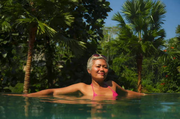 Atractiva y feliz de mediana edad mujer asiática relajada en el complejo tropical piscina infinita con fondo de selva disfrutando relajado en viaje de vacaciones de lujo — Foto de Stock