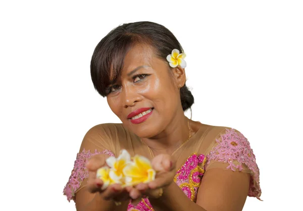 Belle et heureuse femme balinaise indonésienne d'âge moyen en robe de cérémonie traditionnelle souriante et tenant une offrande de fleurs entre ses mains en bienvenue à la religion hindoue de Bali — Photo