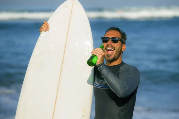 Naturliga porträtt av attraktiva och lyckliga Surfer man på hans 40s redovisade surfbräda efter surfing morgon på vacker strand i våtdräkt dricka ölflaska njuter av sommaren — Stockfoto