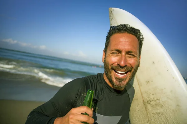 Naturliga porträtt av attraktiva och lyckliga Surfer man på hans 40s redovisade surfbräda efter surfing morgon på vacker strand i våtdräkt dricka ölflaska njuter av sommaren — Stockfoto