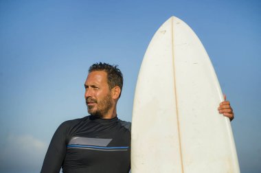 Neoprene mayo giymiş yakışıklı ve çekici bir sörfçü elinde sörf tahtası, yaz sporu ve tatillerin tadını çıkardıktan sonra havalı poz veriyor.