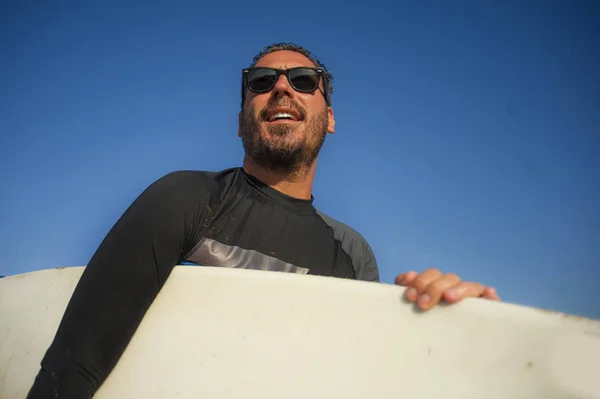 Snygg och attraktiv surfare man i neopren baddräkt redovisade surfbräda leende glad och glad efter surfing njuter sommar vattensport och helgdagar — Stockfoto