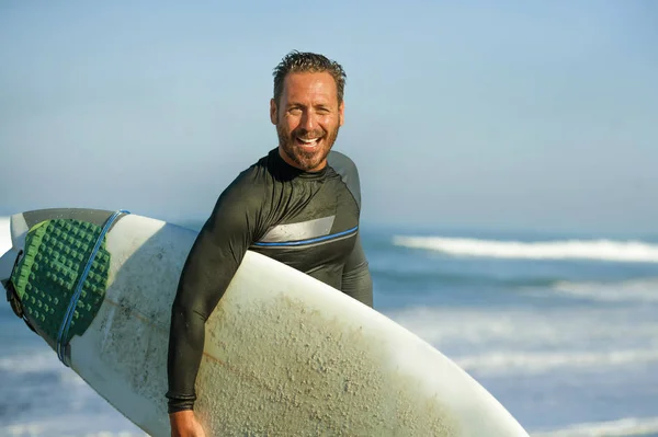 Snygg och attraktiv surfare man i neopren baddräkt redovisade surfbräda leende glad och glad efter surfing njuter sommar vattensport och helgdagar — Stockfoto