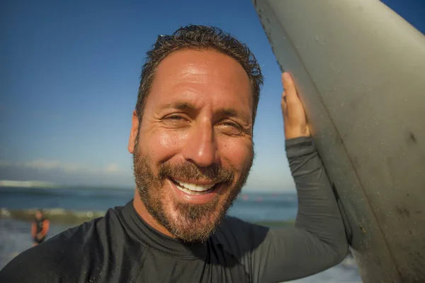 Lifestyle Beach närbild porträtt av stilig och attraktiv surfare man i neopren baddräkt innehav surfbräda poserar sval efter surfing njuter av sommaren — Stockfoto