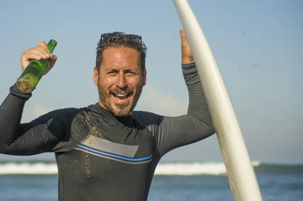 Livsstil porträtt av attraktiva och Happy Surfer man 3os till 40s i neopren surfing baddräkt poserar med surfbräda på stranden njuter vattensport och sommarlov — Stockfoto