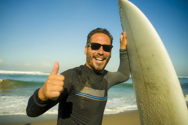 Livsstil porträtt av attraktiva och Happy Surfer man 3os till 40s i neopren surfing baddräkt poserar med surfbräda på stranden njuter vattensport och sommarlov — Stockfoto