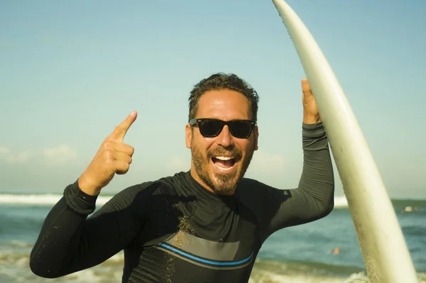 Livsstil porträtt av attraktiva och Happy Surfer man 3os till 40s i neopren surfing baddräkt poserar med surfbräda på stranden njuter vattensport och sommarlov — Stockfoto