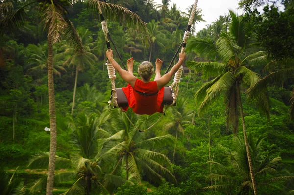 Back retrato de atraente feliz mulher de meia-idade com cabelos grisalhos cavalgando floresta tropical swing despreocupado balançando e desfrutando de aventura na selva tropical sentindo-se livre — Fotografia de Stock