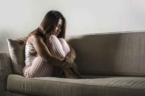 Nuori surullinen ja masentunut aasialainen indonesialainen nainen istuu kotona sohvalla itkien turhautunut ja järkyttynyt kärsimystä stressiä ja masennusta hajoamisen jälkeen — kuvapankkivalokuva