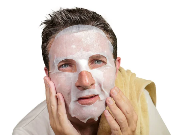 Giovane uomo attraente e felice utilizzando la maschera facciale di carta di bellezza toccare il viso guardando allo specchio sorridente allegro nella bellezza maschile e la cura della pelle — Foto Stock