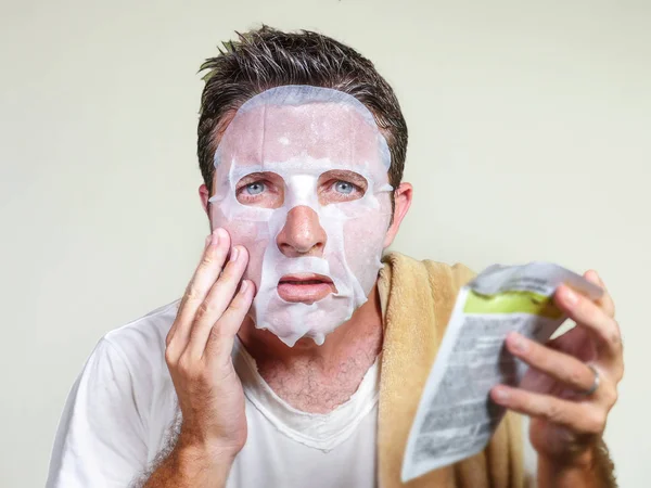 Νέος περίεργος και αστείος άνθρωπος στο σπίτι προσπαθεί χρησιμοποιώντας χαρτί ομορφιάς καθαρισμού μάσκα προσώπου εκμάθηση αντι γήρανση θεραπεία προσώπου ανάγνωση των οδηγιών του προϊόντος στο μπάνιο — Φωτογραφία Αρχείου