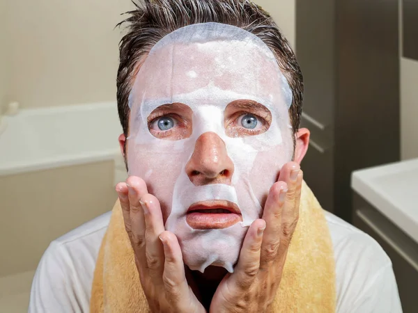 Pemuda aneh dan lucu di rumah mencoba menggunakan kecantikan kertas masker wajah membersihkan belajar anti penuaan pengobatan dalam terkejut ekspresi wajah melihat di cermin — Stok Foto