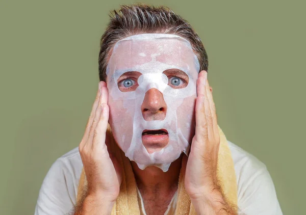 lifestyle isolated background portrait of young weird and funny man at home trying using beauty paper facial mask cleansing learning anti aging treatment