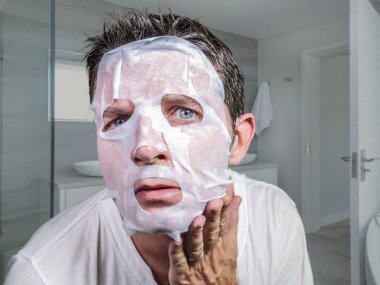 Genç, komik ve dağınık bir adam güzellik maskesi takıyor. Aynaya bakıyor. Cilt bakımı konsepti ve erkek estetik tedavisi karşısında şaşırmış ve dehşete düşmüş.