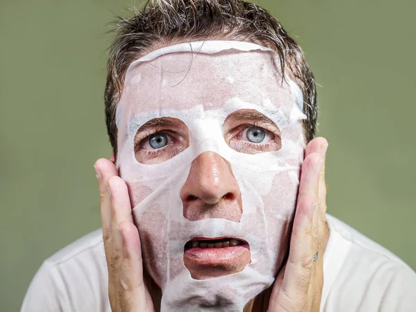 Retrato de jovem estranho e engraçado homem em casa tentando usar papel de beleza máscara facial limpeza aprendizagem anti envelhecimento tratamento na expressão facial concentrada — Fotografia de Stock