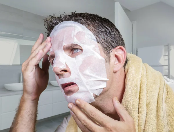 Portret młodego dziwny i zabawny człowiek w domu próbuje za pomocą maski do twarzy kosmetyczne oczyszczanie uczenia się anty starzenie się leczenia w skoncentrowanej ekspresji twarzy — Zdjęcie stockowe