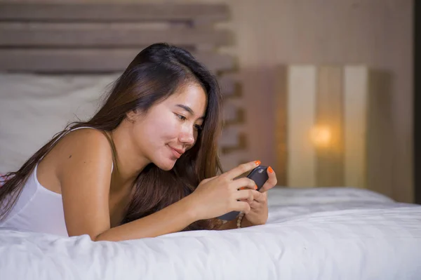 Joven atractiva y feliz adolescente mujer acostada relajada y sonriente alegre en la cama utilizando las redes sociales de Internet o en línea citas aplicación con teléfono móvil en casa — Foto de Stock