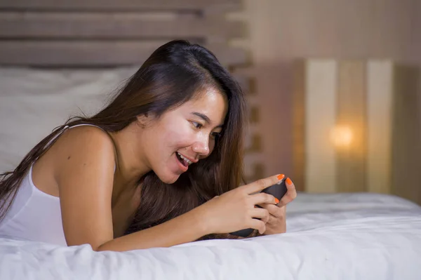 Молодая привлекательная и счастливая женщина-подросток лежала расслабленной и улыбаясь весело в постели с помощью интернета социальные сети или онлайн знакомства приложение с мобильного телефона дома — стоковое фото