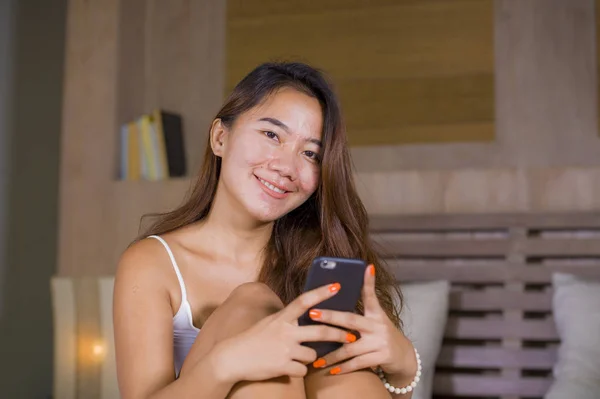 young attractive and happy teenager woman lying relaxed and smiling cheerful in bed using internet social media or online dating app with mobile phone at home