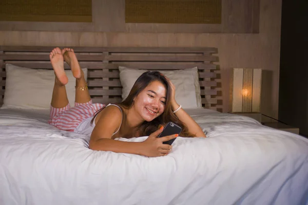 young attractive and happy teenager woman lying relaxed and smiling cheerful in bed using internet social media or online dating app with mobile phone at home