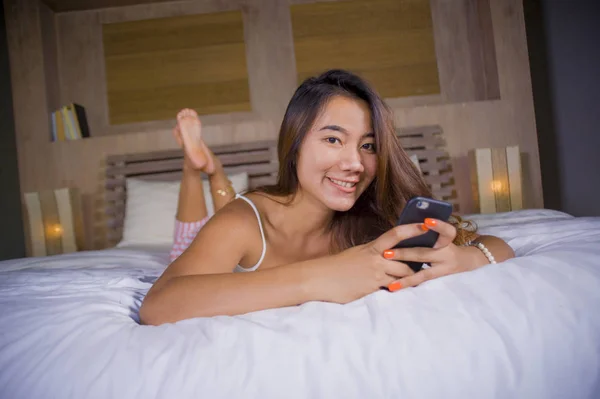 Young attractive and happy teenager woman lying relaxed and smiling cheerful in bed using internet social media or online dating app with mobile phone at home — 스톡 사진