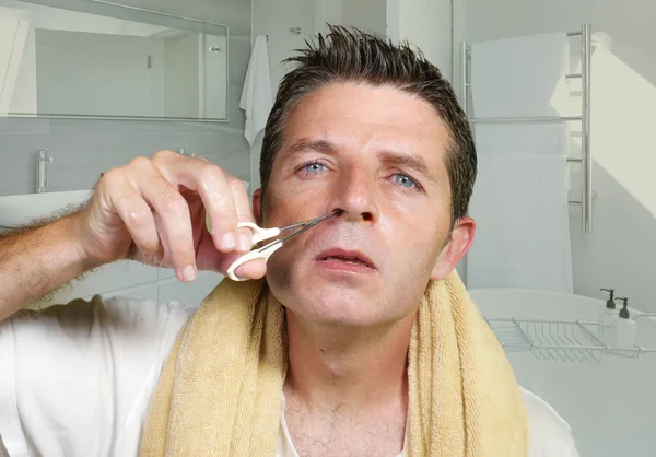 Gaya hidup potret alami pemuda menarik dan terkonsentrasi laki-laki memotong rambut dengan hati-hati di hidungnya dengan gunting kecil di kamar mandi rumah tangga dalam keindahan laki-laki dan kebersihan rumah tangga — Stok Foto