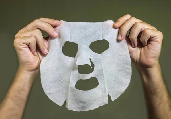 Mužové ruce držící krásný papír obličejový maska izolovaný na sudém pozadí v obličeji koncepce péče o pokožku — Stock fotografie