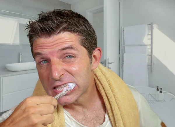 Estilo de vida natural retrato de joven atractivo y feliz hombre caucásico en el baño de casa lavándose el diente con cepillo de dientes mirando en el espejo en el cuidado dental — Foto de Stock