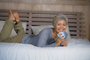 kız ağarmış çekici ve başarılı olgun kadın yatakta oturmuş kahve içiyor rahat, orta yaşlı kadın olarak mutlu gülümsüyor ev selyaşam tarzının tadını çıkarıyor