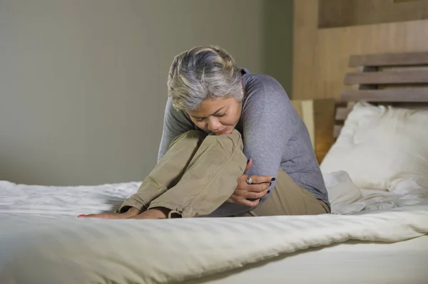 Deprimida y triste pelo gris mujer madura llorando sola sentada en la cama sufriendo crisis de dolor y depresión problema sintiéndose perdida y abrumada en casa — Foto de Stock